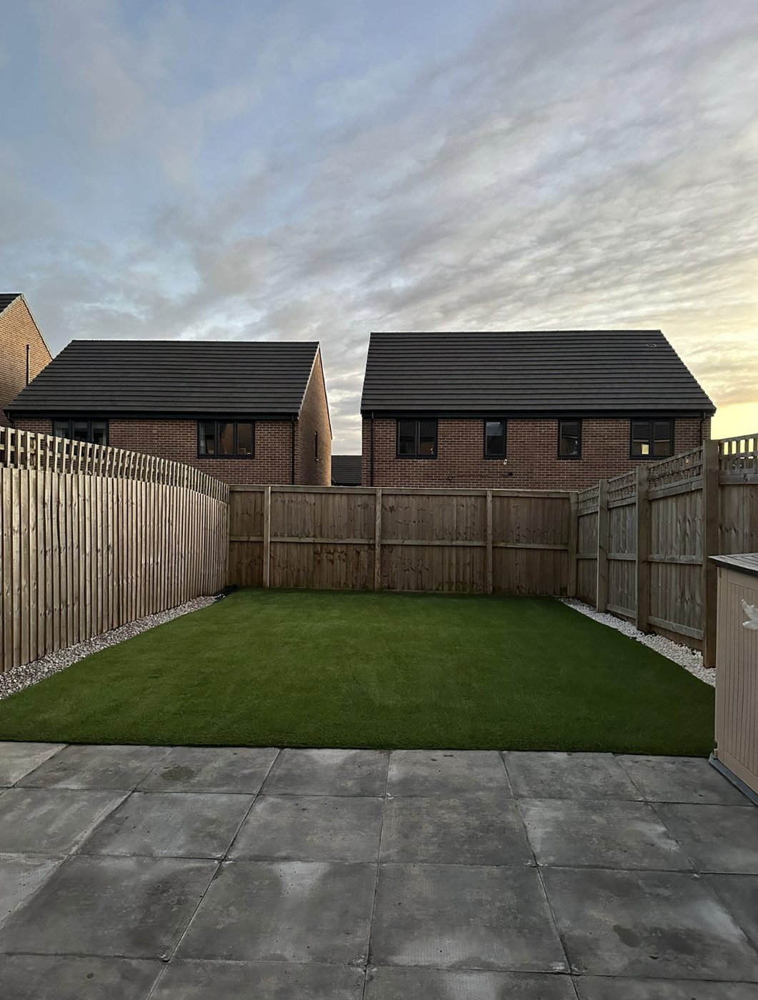 Artificial grass lawn with gravel margins in a new build garden at sunset