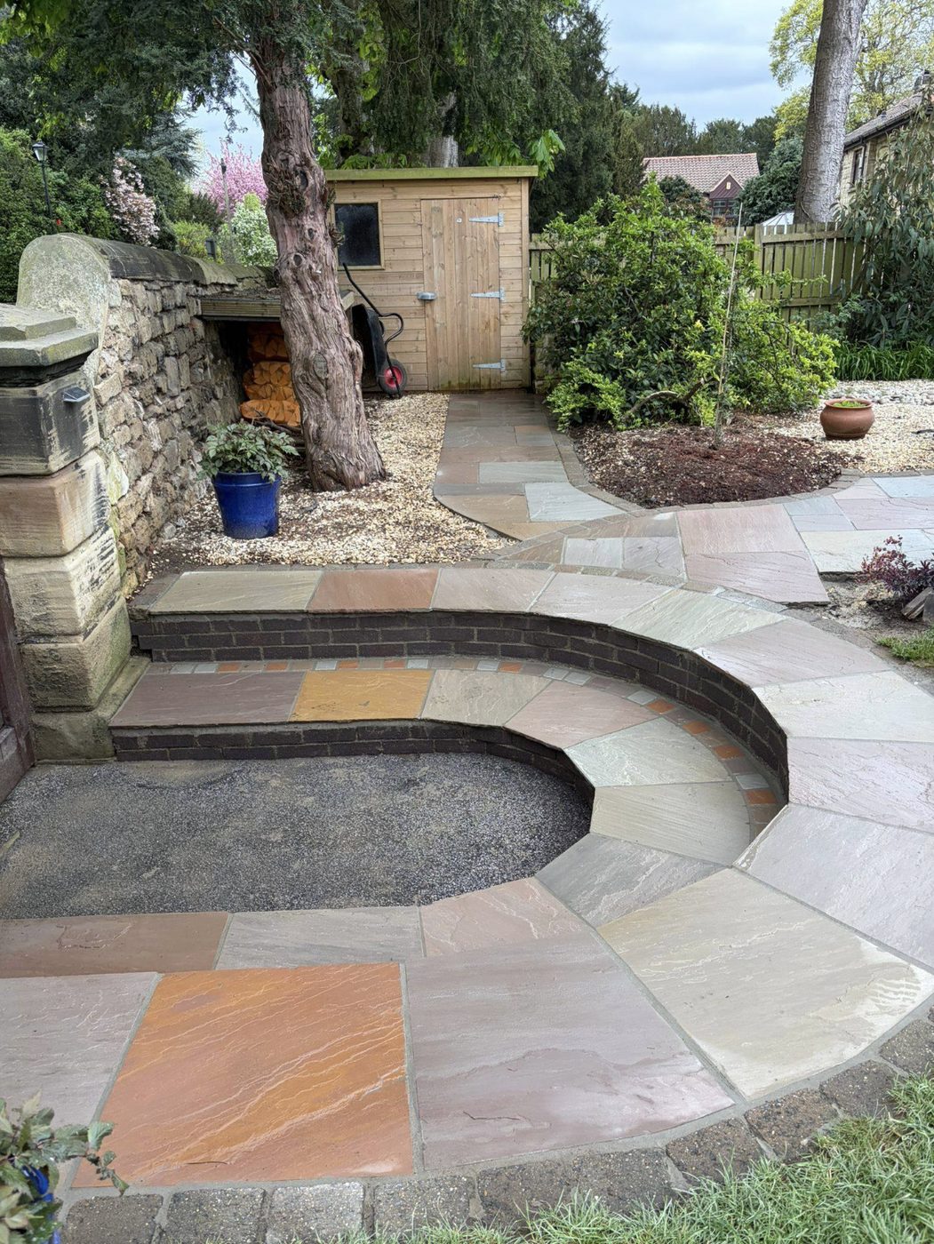 Curved Indian sandstone steps with brick risers leading to a garden shed